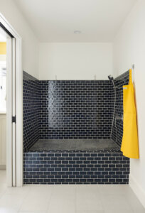 At-home dog wash station. The dog wash is elevated from the floor and features blue tile. On the wall to the left is a pocket door, straight ahead is the dog wash, and on the right is a hook with a yellow apron.