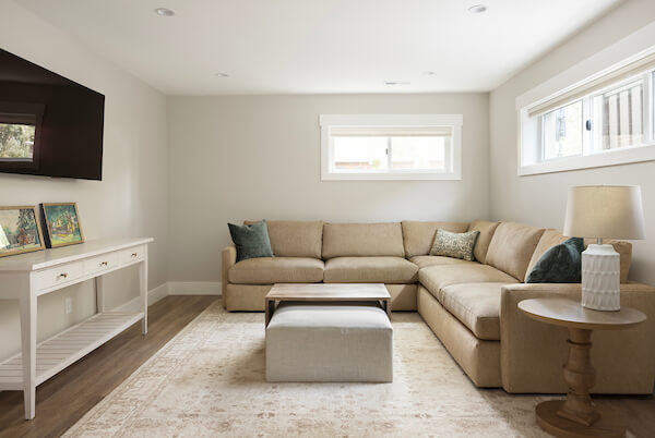 Family room in the basement with an L-shaped couch underneath the windows and with a coffee table and TV in front.