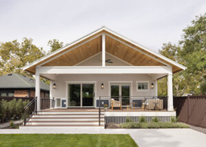 Large, covered deck in the backyard. The space includes two doors with one being from the primary bedroom and the other from the living room, outdoor furniture, and a vaulted ceiling.