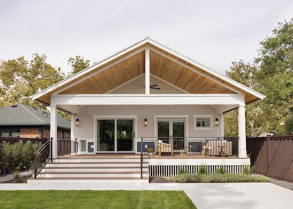 Large, covered deck in the backyard. The space includes two doors with one being from the primary bedroom and the other from the living room, outdoor furniture, and a vaulted ceiling.
