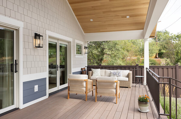 Large, covered deck in the backyard. The space includes two doors with one being from the primary bedroom and the other from the living room, outdoor furniture, and a vaulted ceiling.
