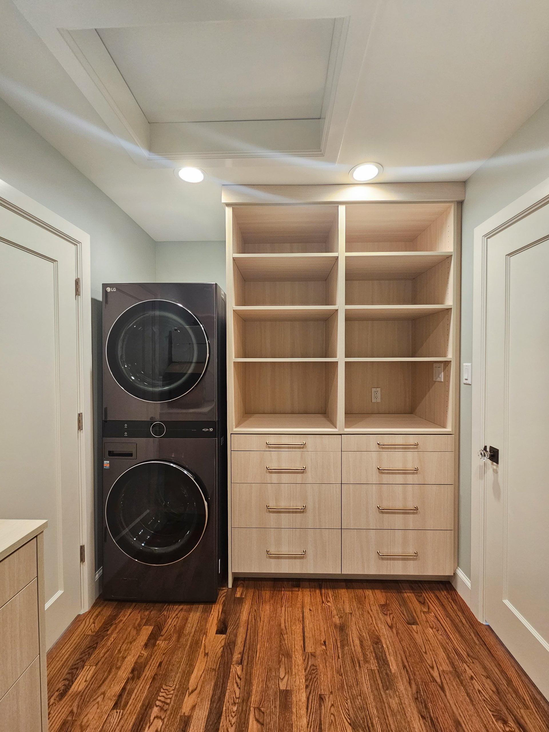 Walk-through closet with hardwood floors, cabinets, and a stacked washer and dryer.