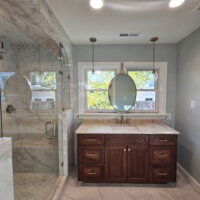Thumbnail of http://Bathroom%20sink%20and%20shower.%20The%20sink%20is%20located%20in%20front%20of%20the%20two%20windows%20with%20a%20mirror%20centered%20between%20and%20lights%20hung%20from%20the%20ceiling%20on%20either%20side.%20The%20shower%20is%20enclosed%20with%20glass%20and%20features%20a%20bench.